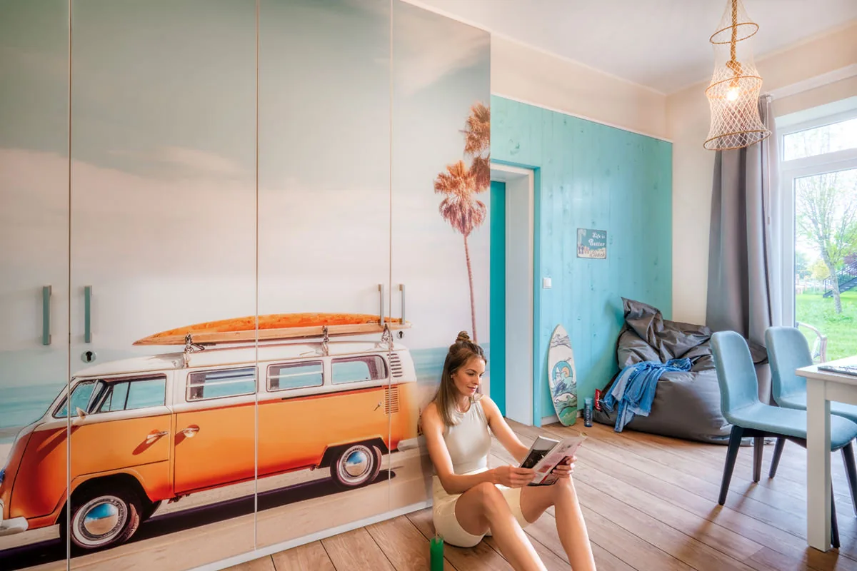 Junge Frau sitzt vor einem Schrank mit VW-Bulli-Motiv im Apartment im Strandstil