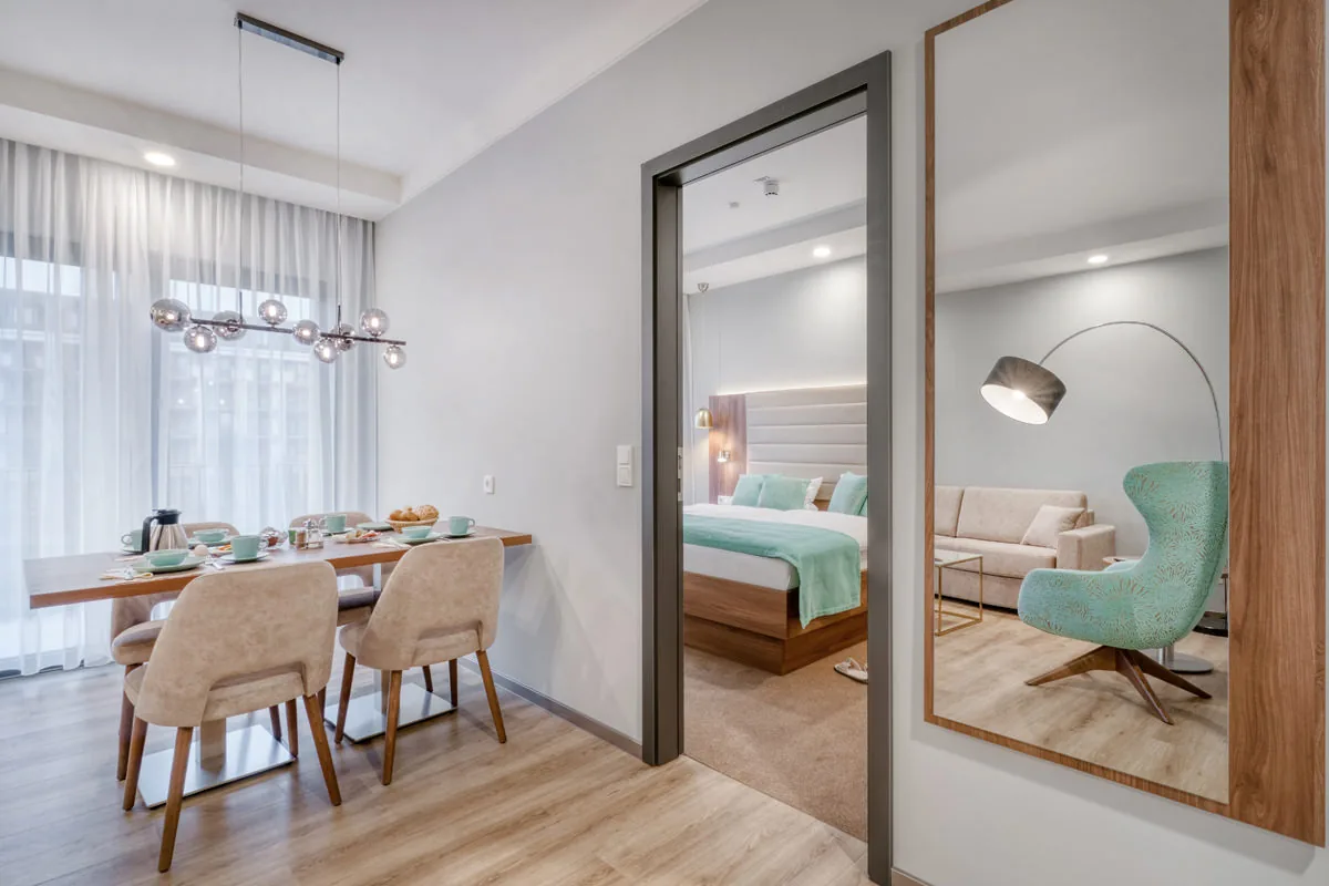 Gedeckter Essplatz im Apartment, im großen Wandspiegel spiegeln sich Schlafbereich und Sessel