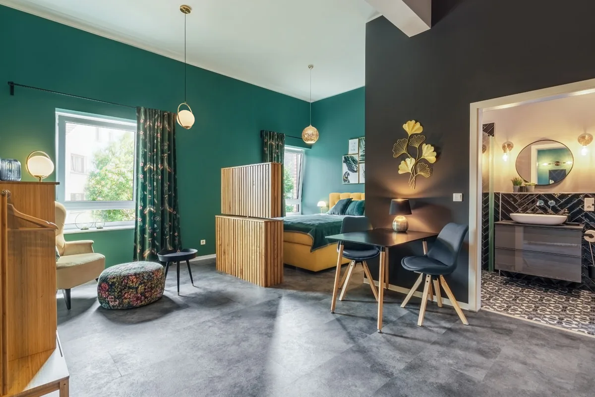 Apartment mit smaragdgrüner Wand, Holzraumteiler vor dem Bett, Essplatz und offenem Bad