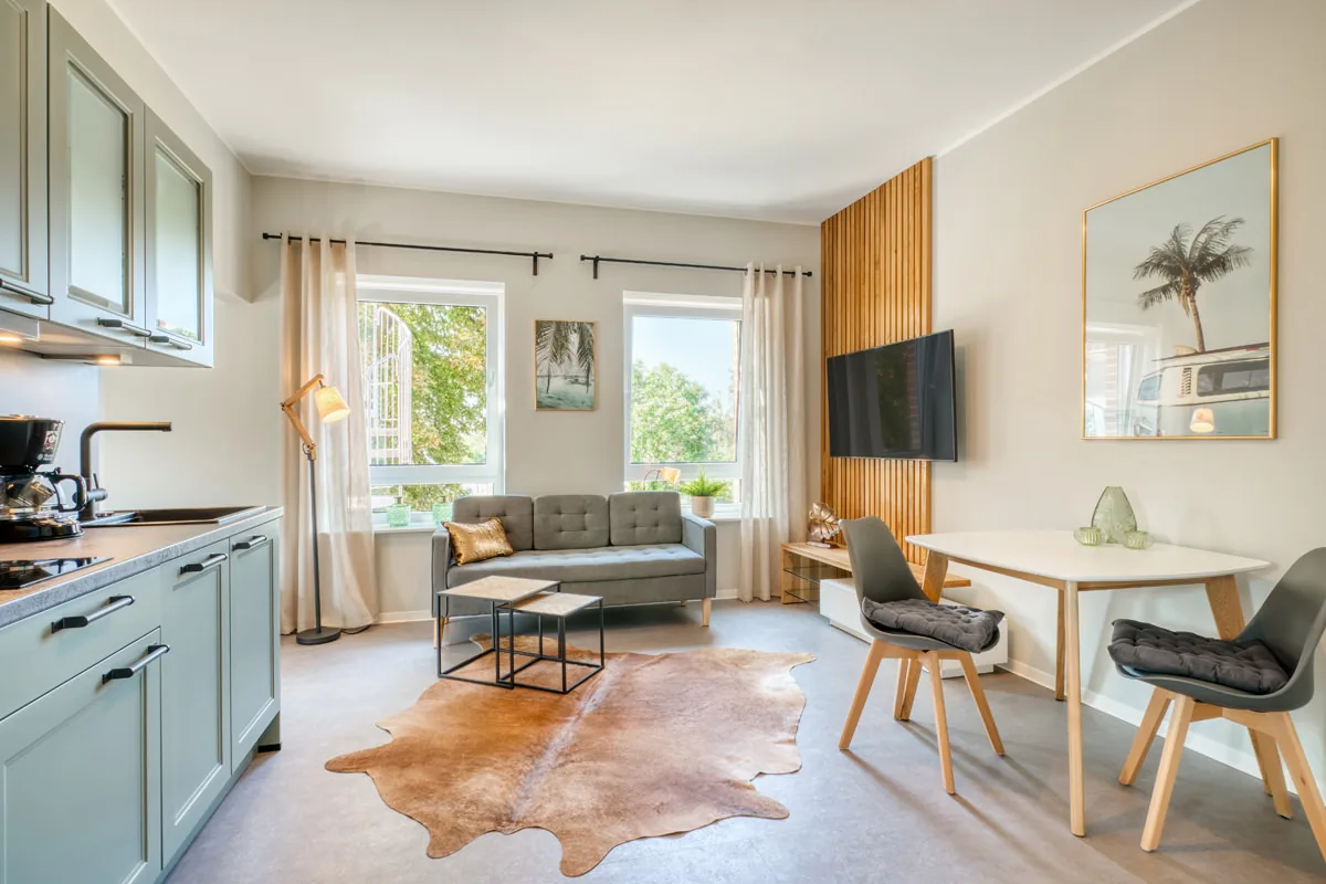 Apartment mit mintgrüner Küchenzeile, Sofa, Kuhfellteppich und Essplatz vor Holzlamellen