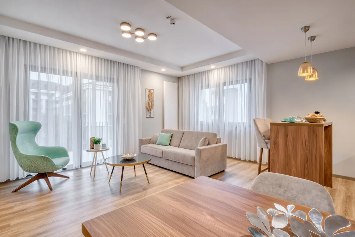 Wohnraum mit Sofa, grünem Sessel und Tresen, im Vordergrund der Esstisch
