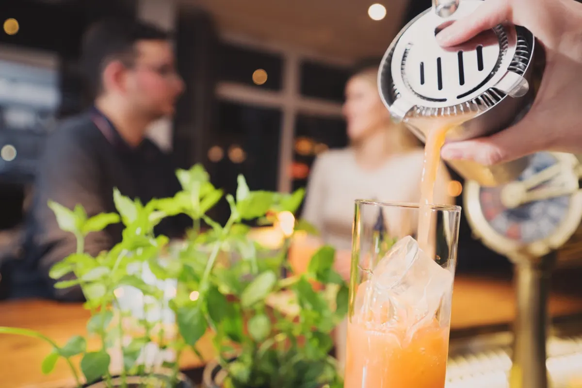 Cocktail being poured at the bar, two guests in the background