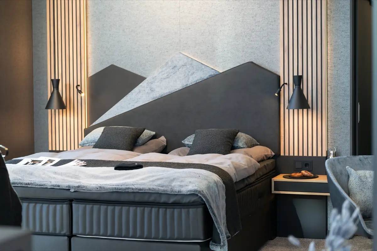 Double bed in front of a headboard shaped like a mountain silhouette, wall lamps either side