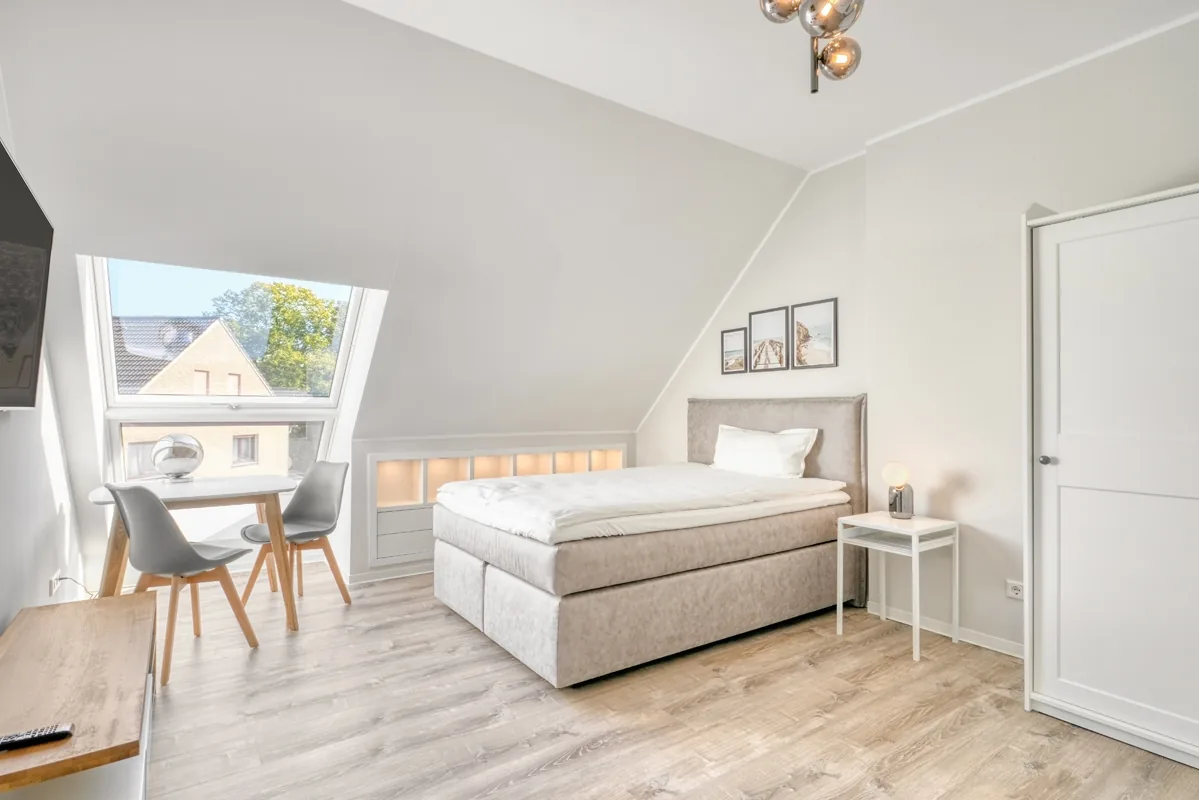 Helles Dachzimmer mit Dachflächenfenster, kleiner Sitzgruppe und Bett unter der Schräge