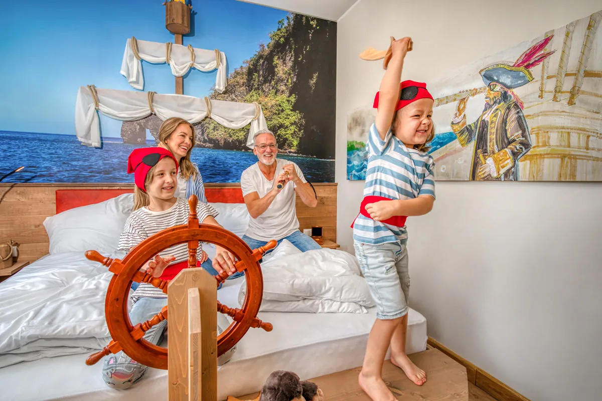 Familie im Piraten-Themenzimmer – Kind mit Holzschwert, Steuerrad und Wandbild eines Segelschiffs
