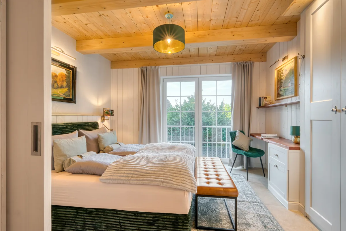 Schlafzimmer im Ferienhaus mit Holzbalkendecke, grünem Bettsockel und Balkontür ins Grüne