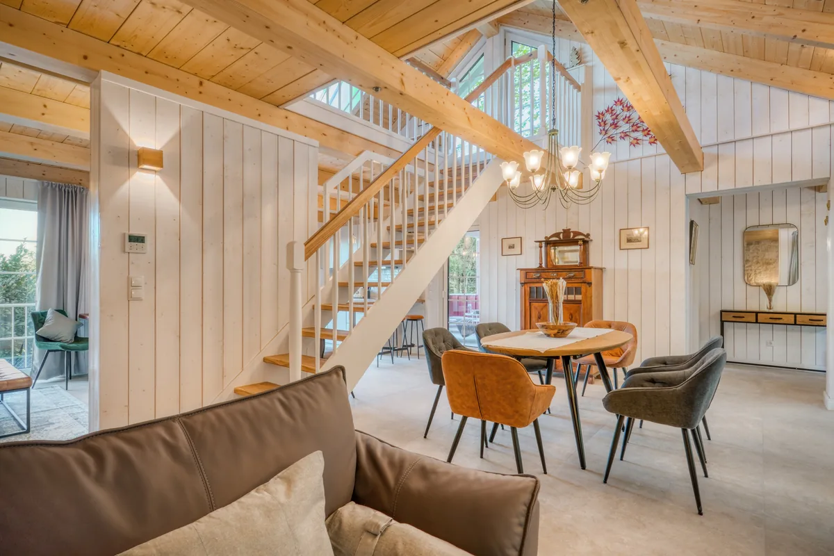 Wohnraum im Ferienhaus mit offener Galerietreppe, Kronleuchter und rundem Esstisch