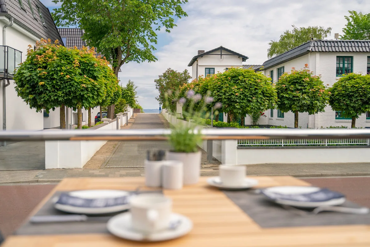 Gedeckter Frühstückstisch auf dem Balkon mit Blick durch die Baumallee zum Wasser