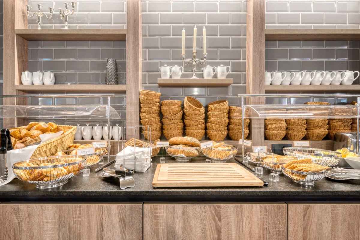 Frühstücksbuffet mit Körben voller Gebäck, gestapelten Tassen und Kerzenleuchter