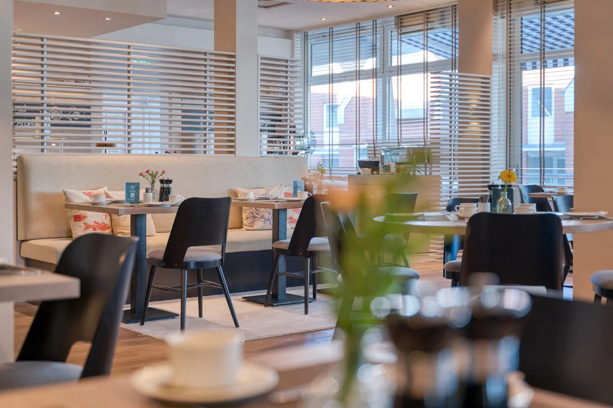 Blick über einen gedeckten Tisch in den Frühstücksraum mit Bank und Holzjalousien