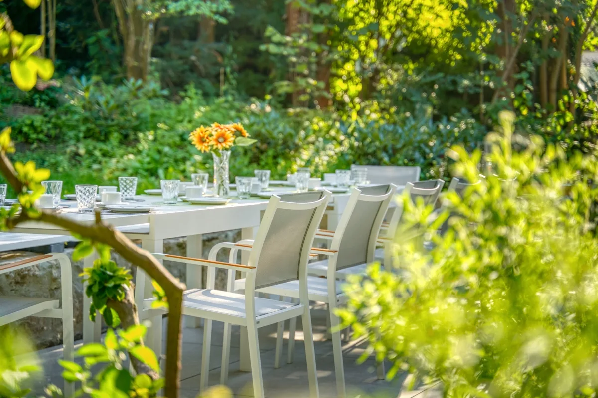Gedeckter Tisch auf der Gartenterrasse – Sonnenblumen, Sonnenlicht und Grün ringsum