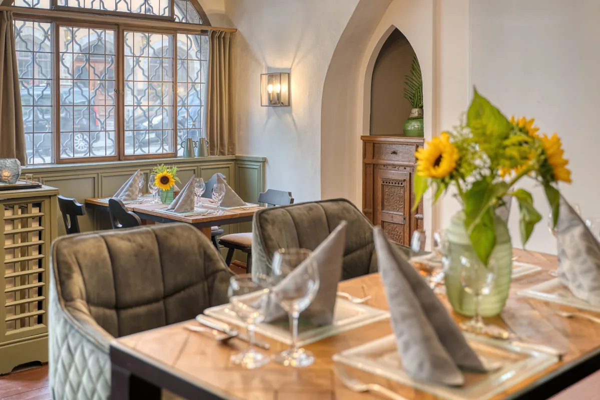 Eingedeckter Tisch mit Sonnenblumen im historischen Gastraum, Rundbogendurchgang dahinter