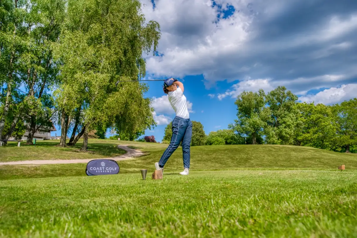 Golfer teeing off beside the banner of a golf academy