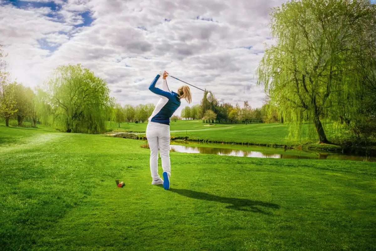 Golfer teeing off in front of weeping willows and a pond