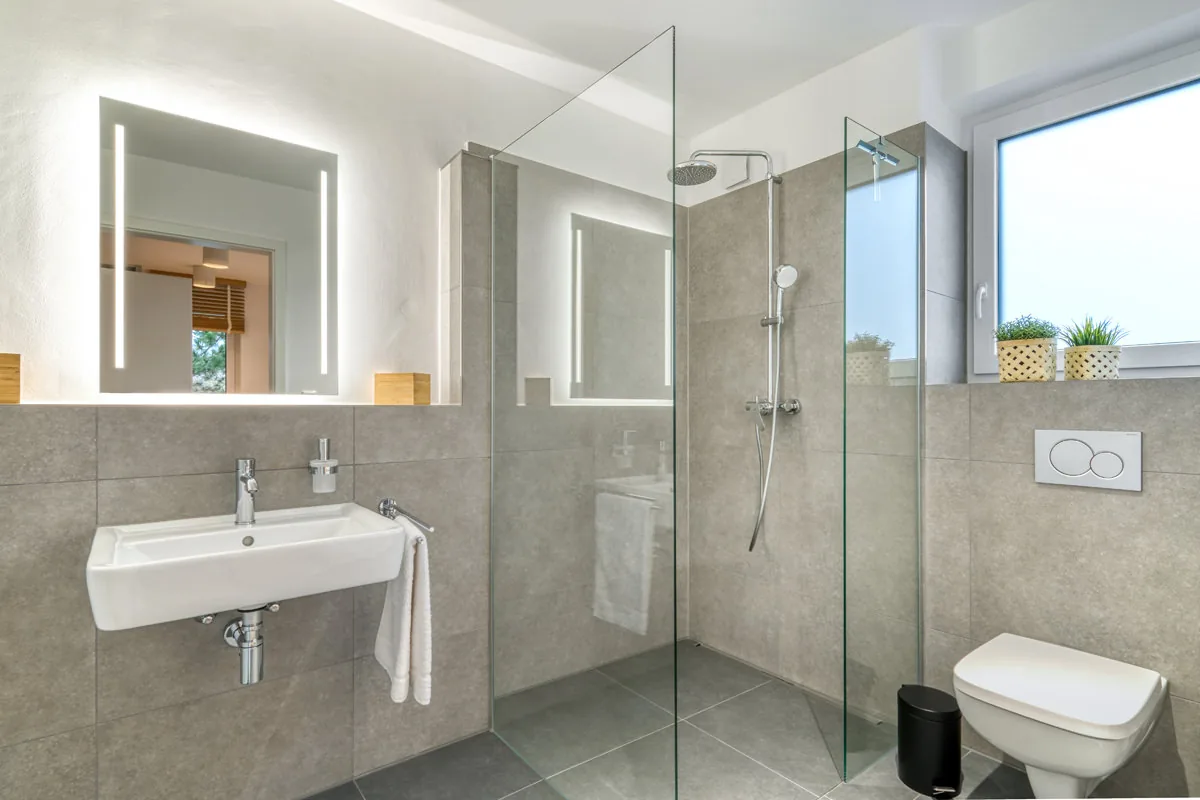 Badezimmer in Grautönen mit bodengleicher Walk-in-Dusche, Waschbecken und Tageslichtfenster