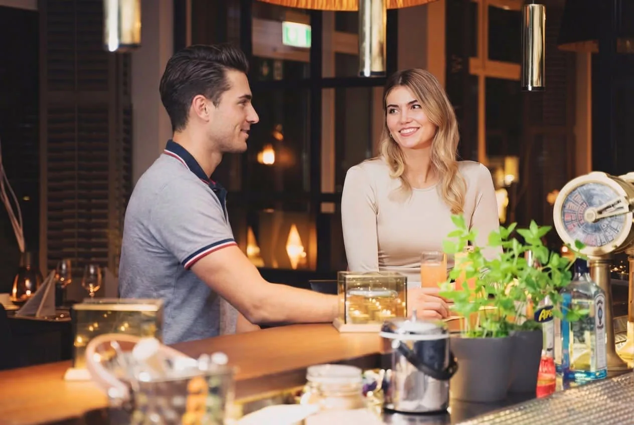 Zwei Gäste im Gespräch an der Hotelbar, im Vordergrund frische Minze und Gläser