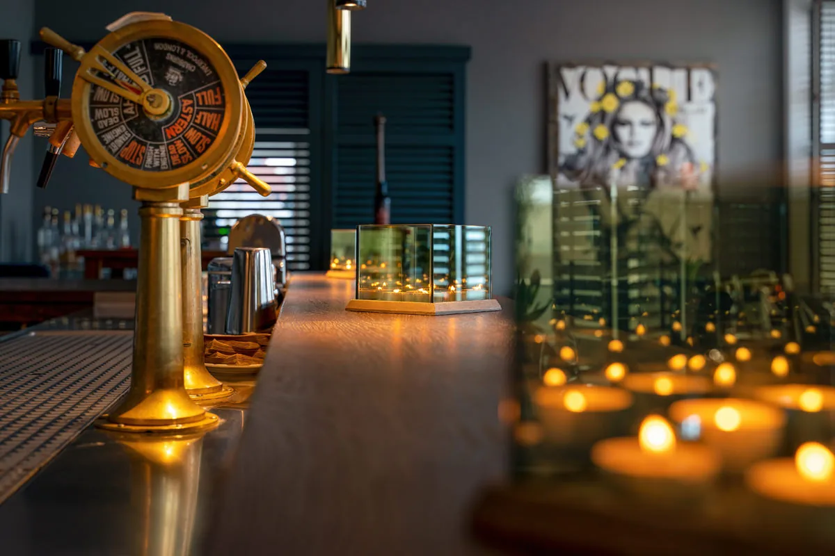 Hotelbar bei Abendlicht – historischer Messingzapfhahn, Teelichter und Spiegelungen auf dem Tresen