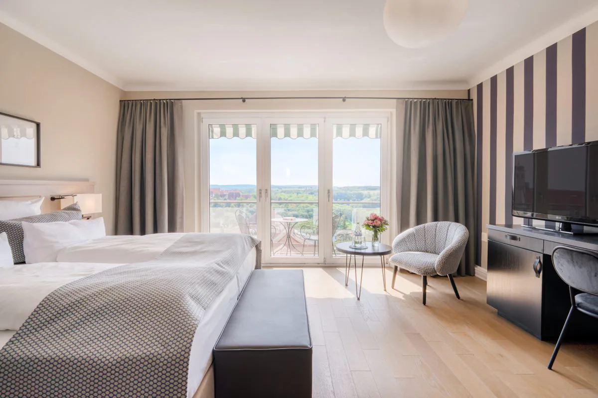 Hotelzimmer mit Doppelbett, Sessel und Balkontür mit Blick über Felder und Wald