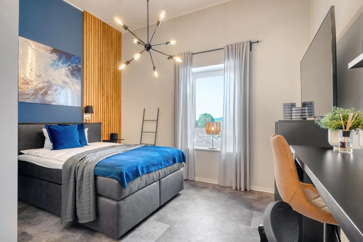 Hotelzimmer mit blauem Wandbild, Holzlamellen und Sputnik-Deckenleuchte über dem Bett