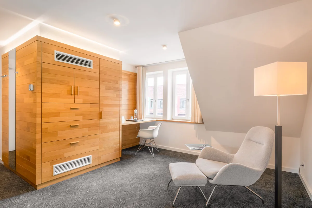 Hotelzimmer unter der Dachschräge mit Sessel, Hocker und raumhohem Holzschrank