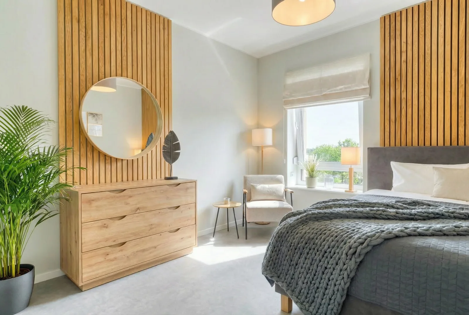 Hotel room with slatted wood wall, gold-framed round mirror above the dresser and knitted throw
