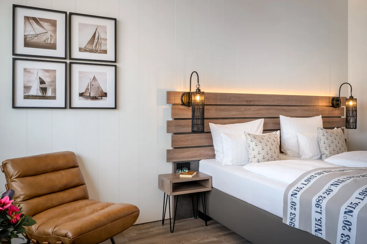 Doppelzimmer im maritimen Stil – Holzkopfteil mit Leselampen, Segelfotografien und Ledersessel