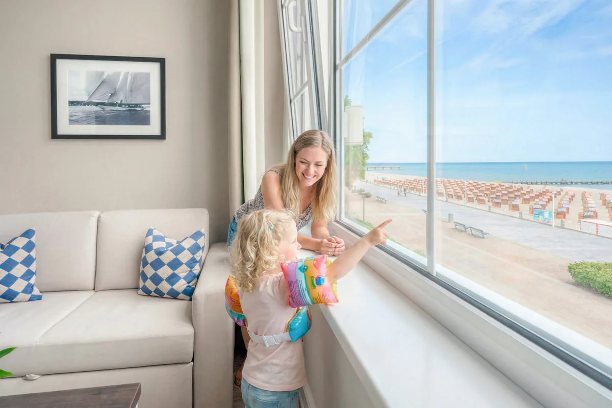 Mutter und Kind am Zimmerfenster mit Blick auf Strandkörbe und Meer