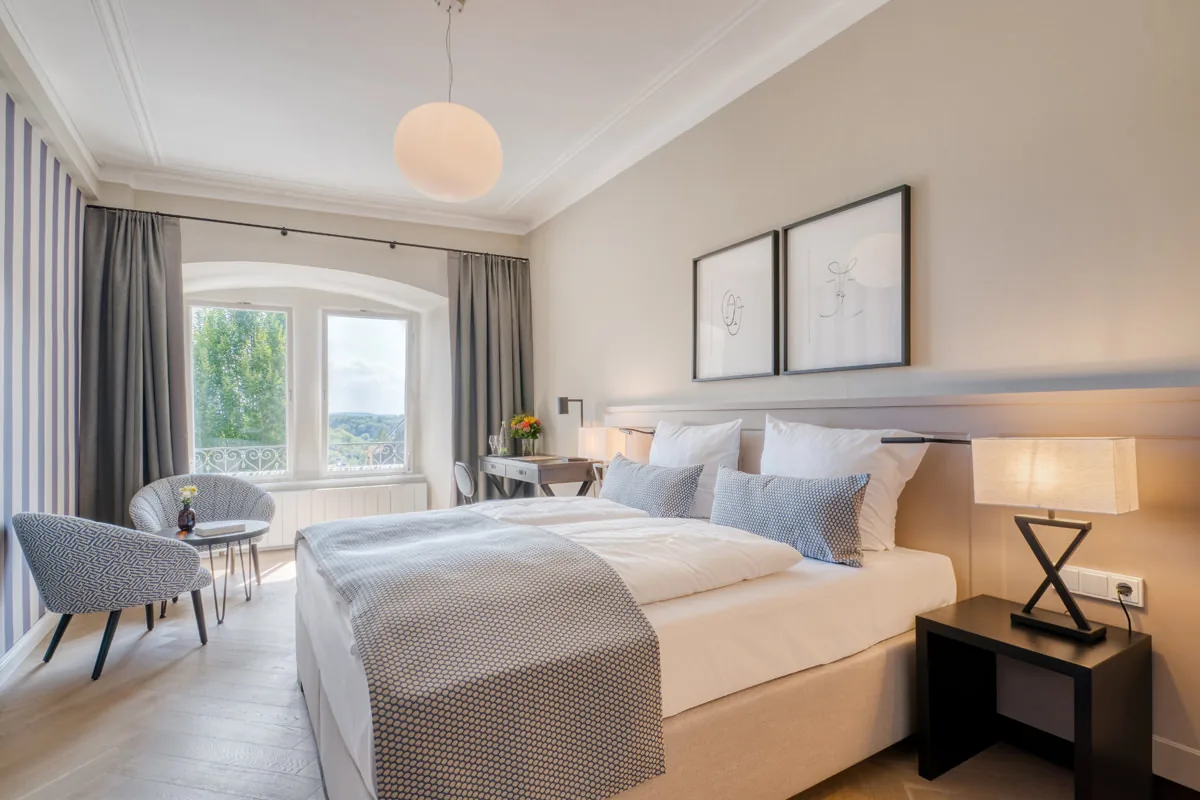 Großes Hotelzimmer mit Sitzecke am Rundbogenfenster, Kugelleuchte und Doppelbett
