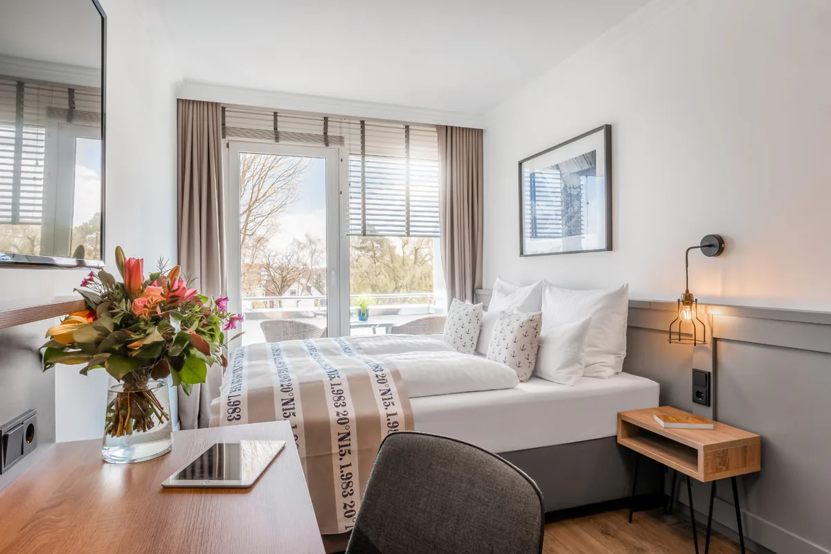 Hotelzimmer mit Schreibtisch, Blumenstrauß und Blick durch die Balkontür ins Grüne