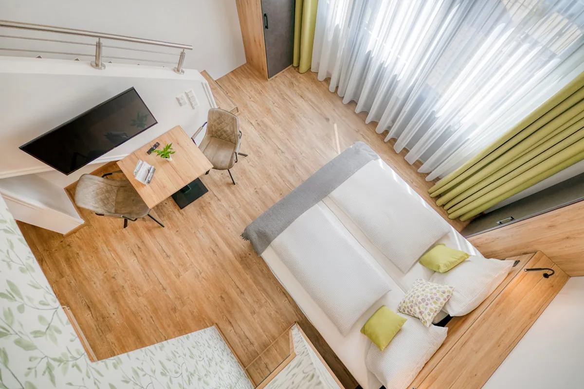 Blick von oben auf ein Hotelzimmer mit Doppelbett, Arbeitsplatz und grünen Vorhängen