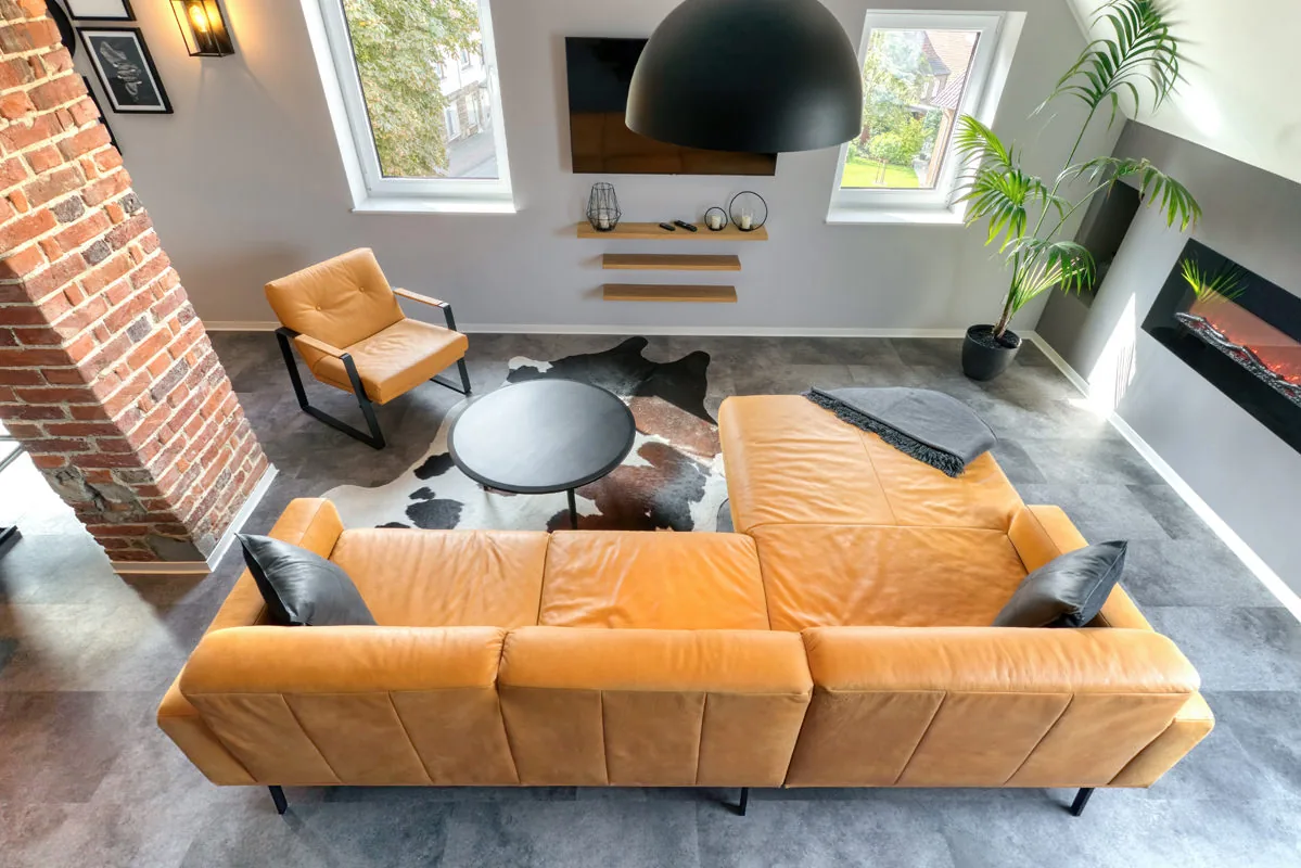 Blick von der Galerie auf orangefarbenes Ledersofa, Kuhfell und Elektrokamin im Loft