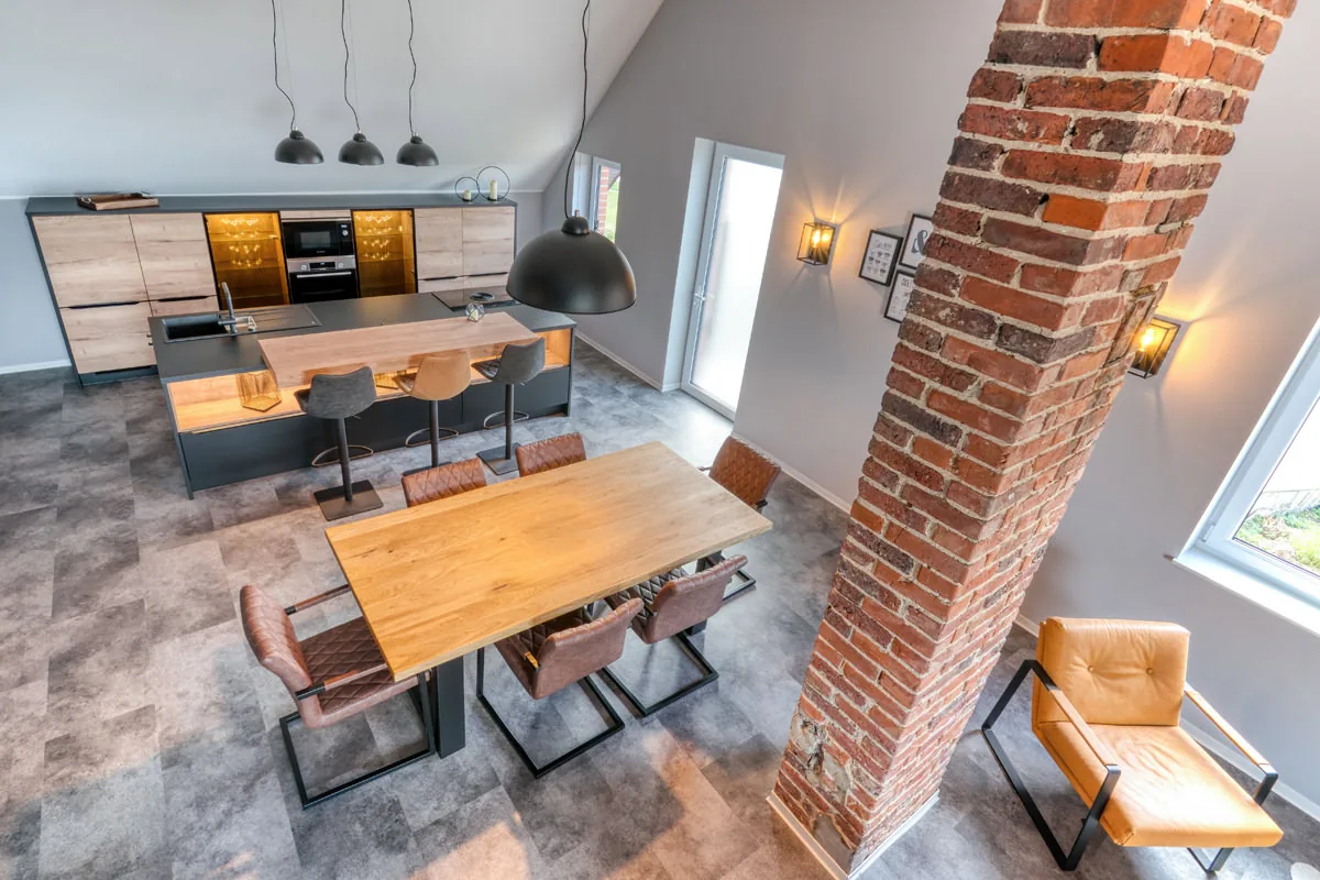Offene Küche und langer Esstisch im Loft, davor ein freistehender Backsteinpfeiler