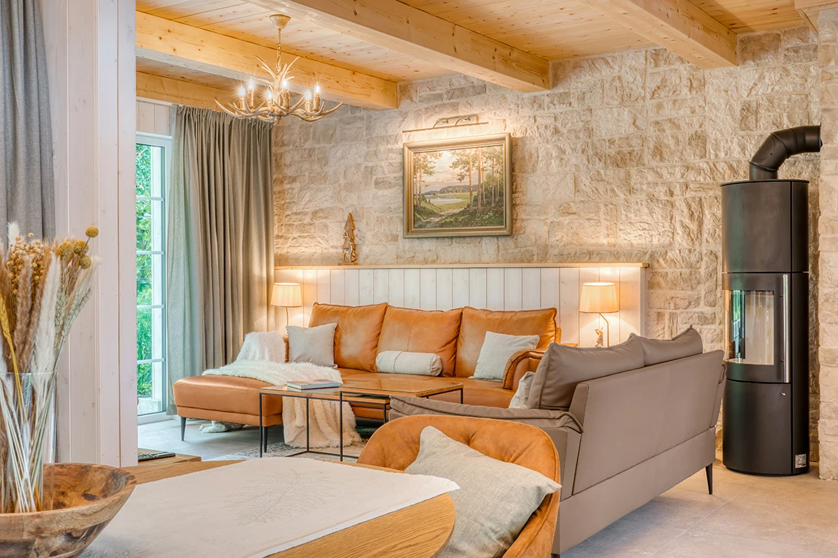 Wohnlounge mit Natursteinwand, Holzbalkendecke, Cognac-Ledersofa und schwarzem Kaminofen