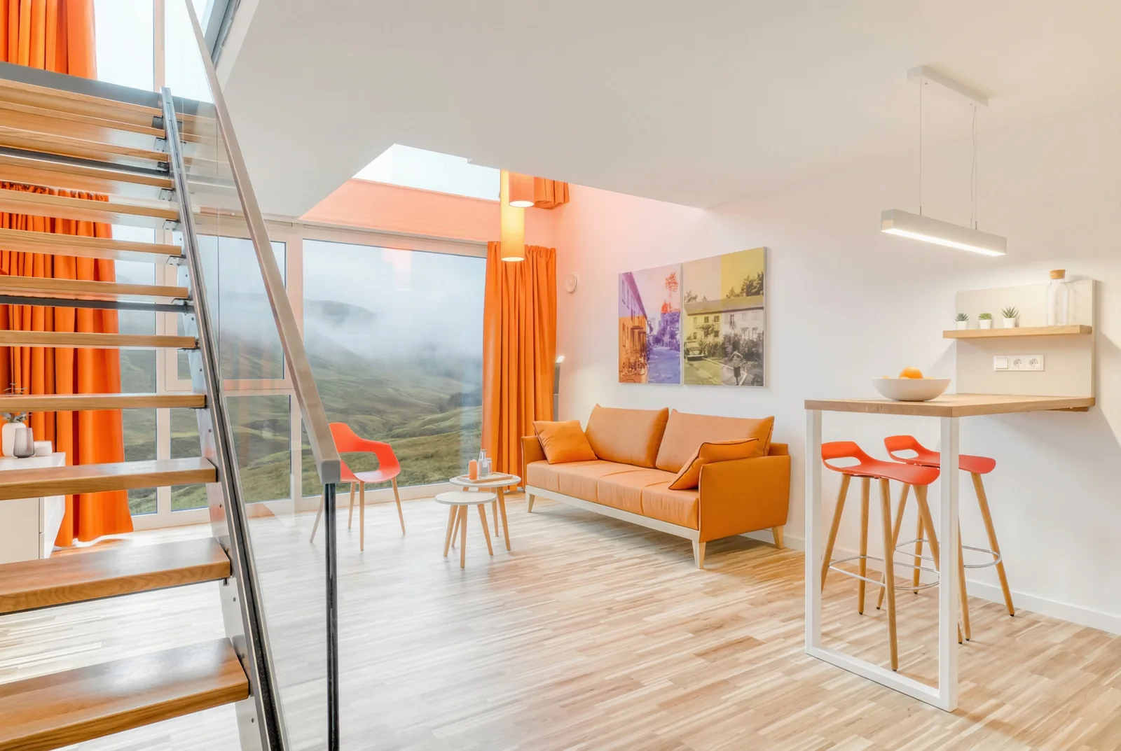 Maisonette apartment with open staircase, orange sofa and a misty mountain view