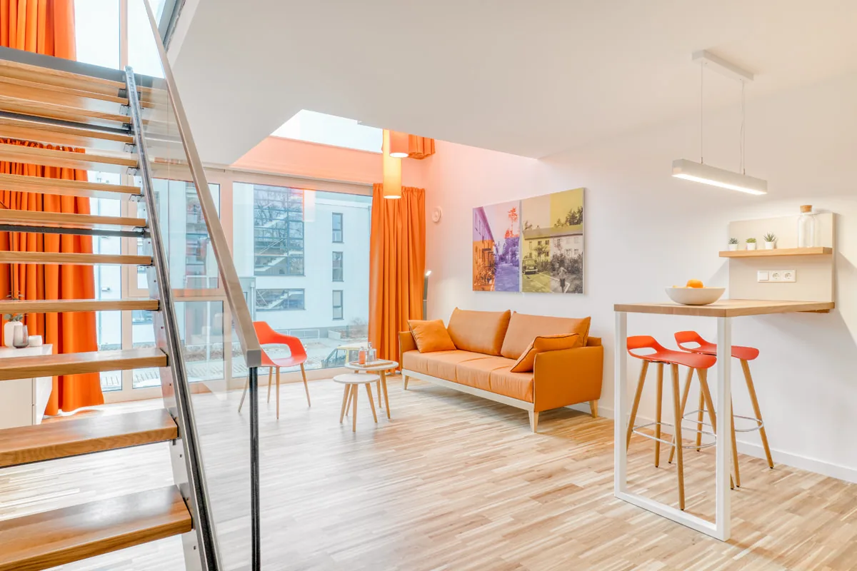 Maisonette-Apartment über zwei Ebenen mit offener Treppe, orangefarbenem Sofa und Bartheke