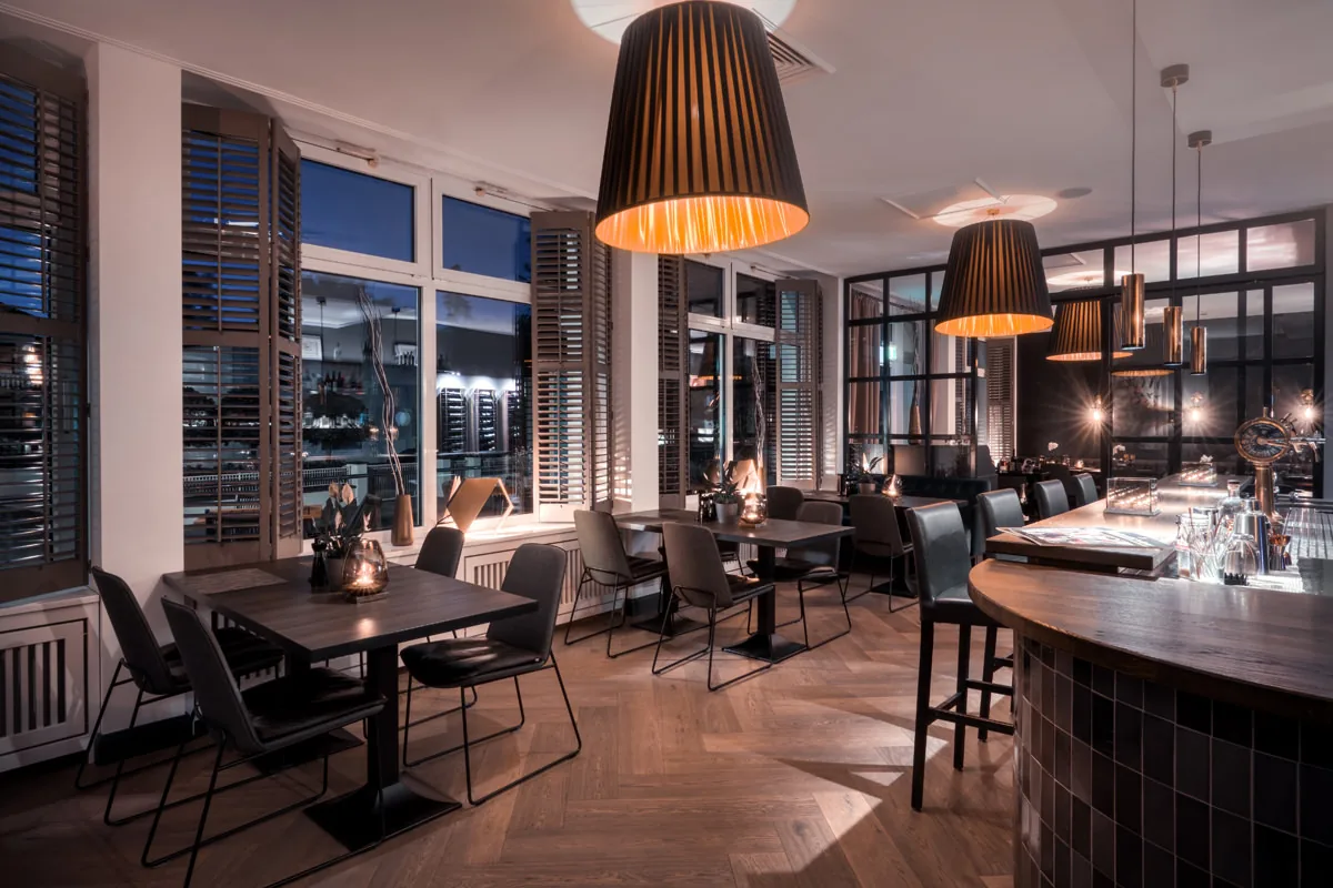 Restaurant zur blauen Stunde – Fensterfront mit Holzläden, Kupferleuchten und Bartresen