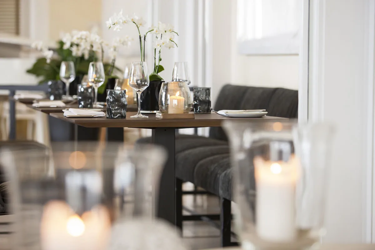 Lange Tafel mit weißen Orchideen und Kerzen, dahinter eine dunkle Polsterbank