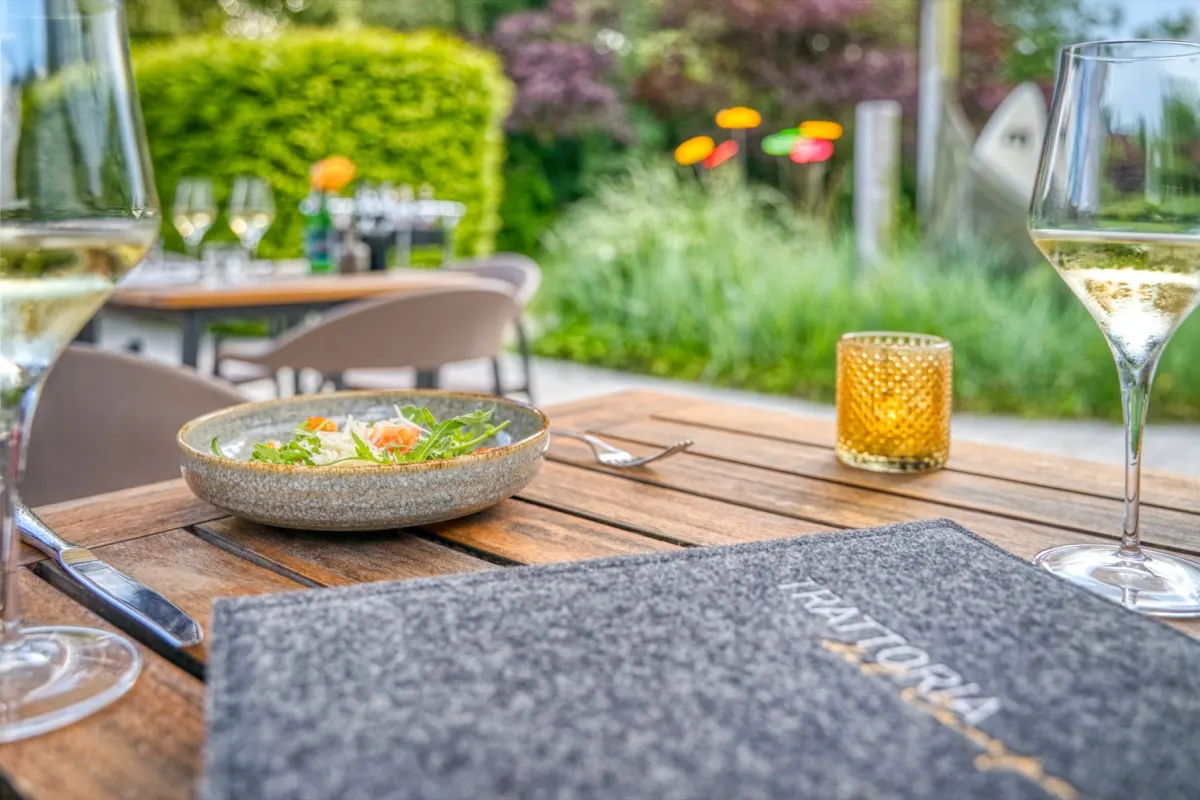 Plated dish and white wine on a terrace table surrounded by greenery