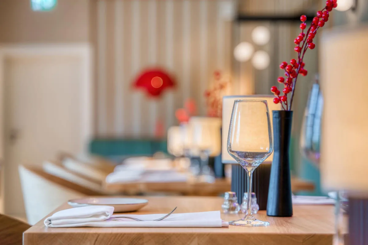 Gedeckter Tisch im Restaurant mit Weinglas und roten Ilexzweigen in schwarzer Vase