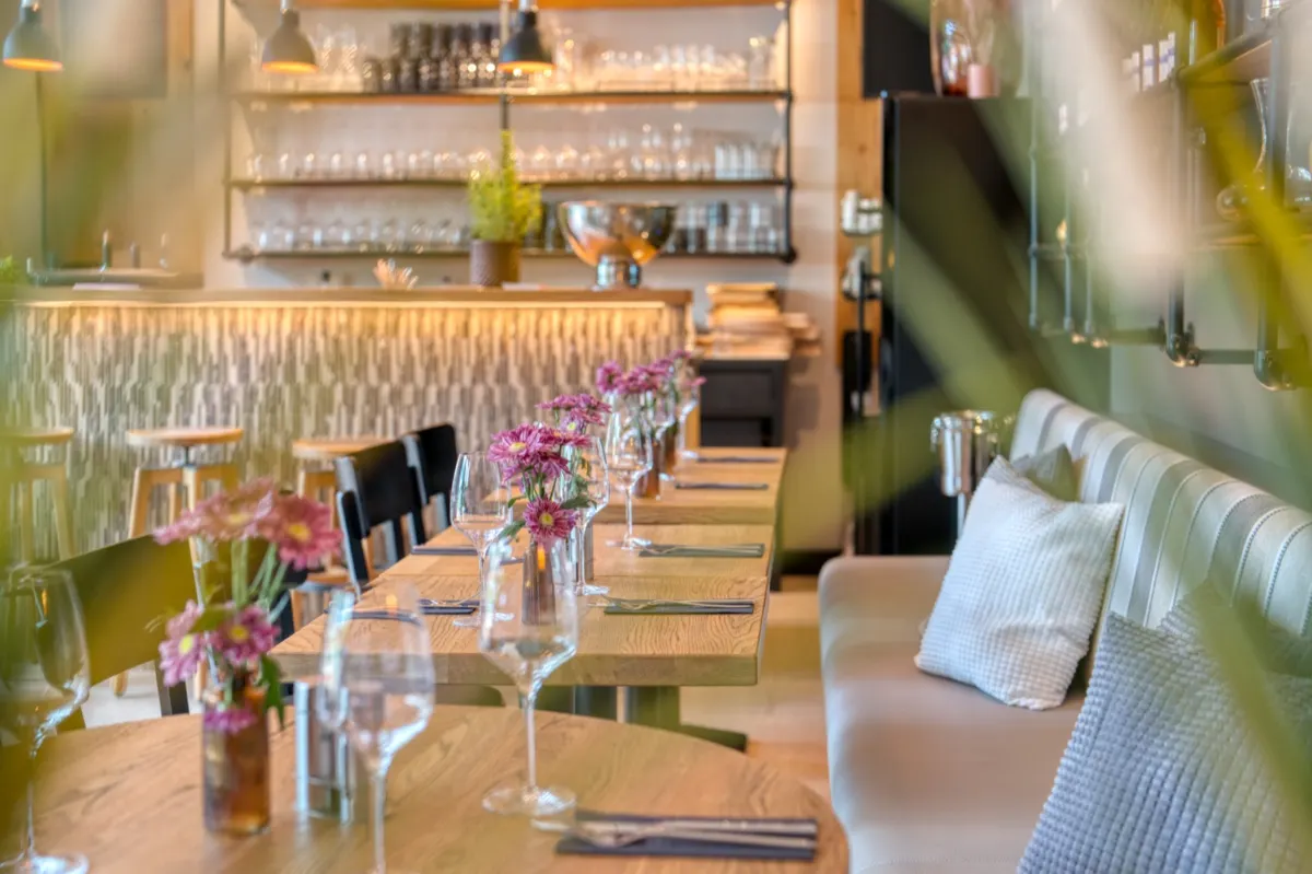Laid restaurant tables with flowers in front of a pale upholstered bench