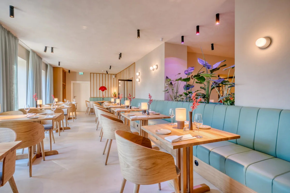 Modernes Restaurant mit türkisfarbener Sitzbank, hellem Holz und großer Pflanzeninsel