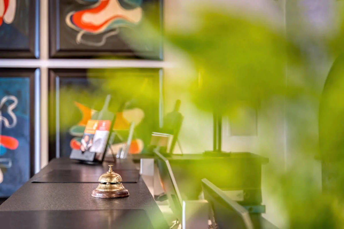 Messing-Tischglocke auf dem Rezeptionstresen, im Hintergrund farbige Kunstdrucke