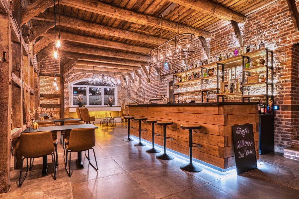 Bar in einer umgebauten Scheune – Fachwerk, Backsteinwände und Holztresen mit Barhockern