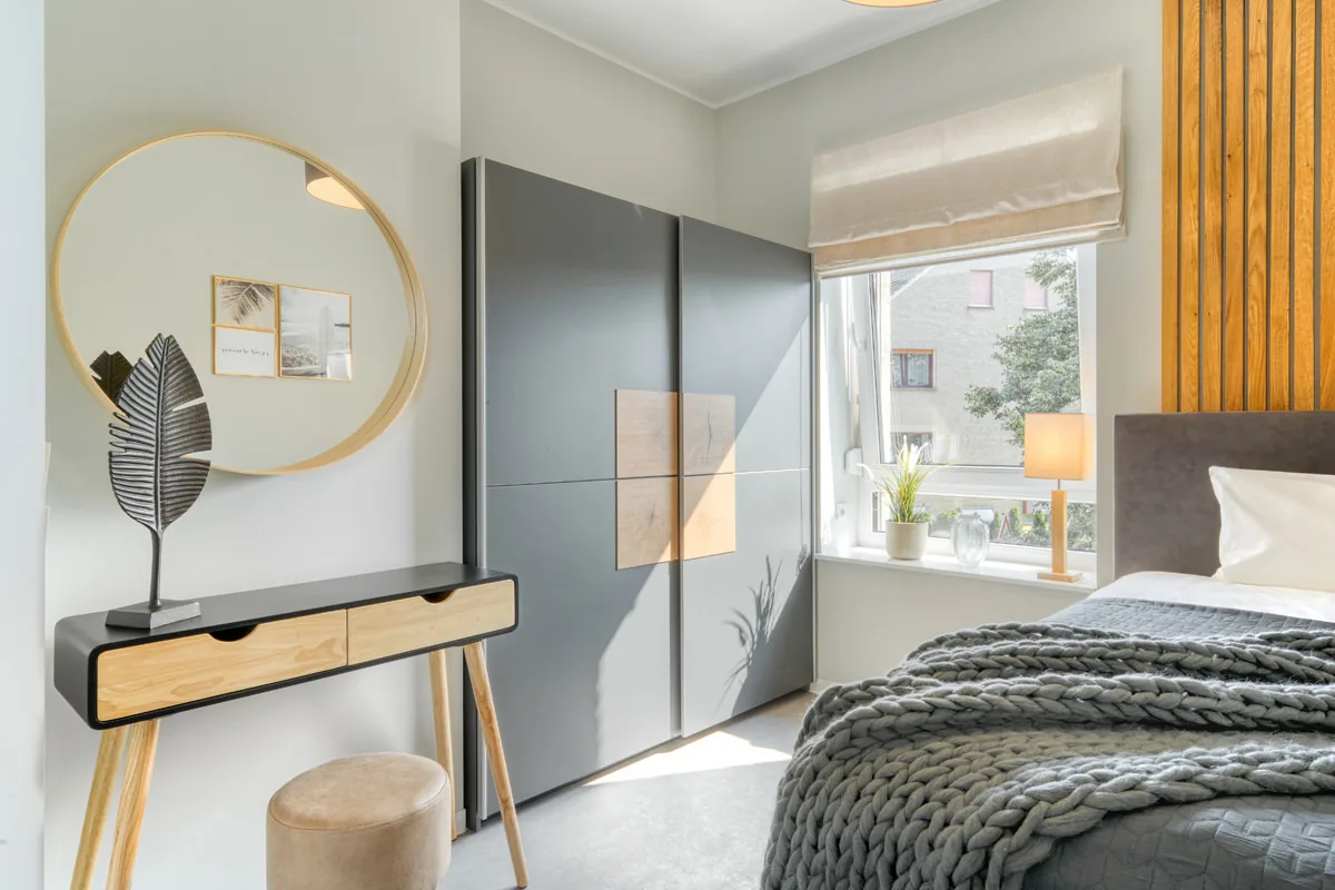 Schlafzimmer mit goldgerahmtem Rundspiegel über schmaler Konsole, Schiebeschrank und Strickdecke