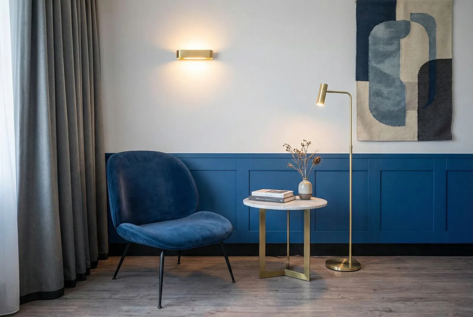 Seating corner with blue velvet chair against blue panelling, brass lights and marble table
