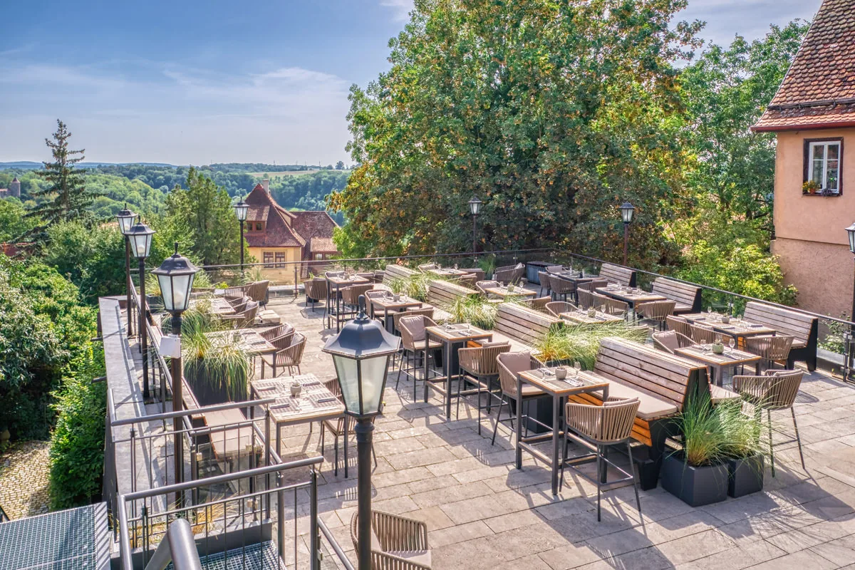 Große Gastterrasse mit Laternen und Gräserkübeln, dahinter der Blick über das Tal