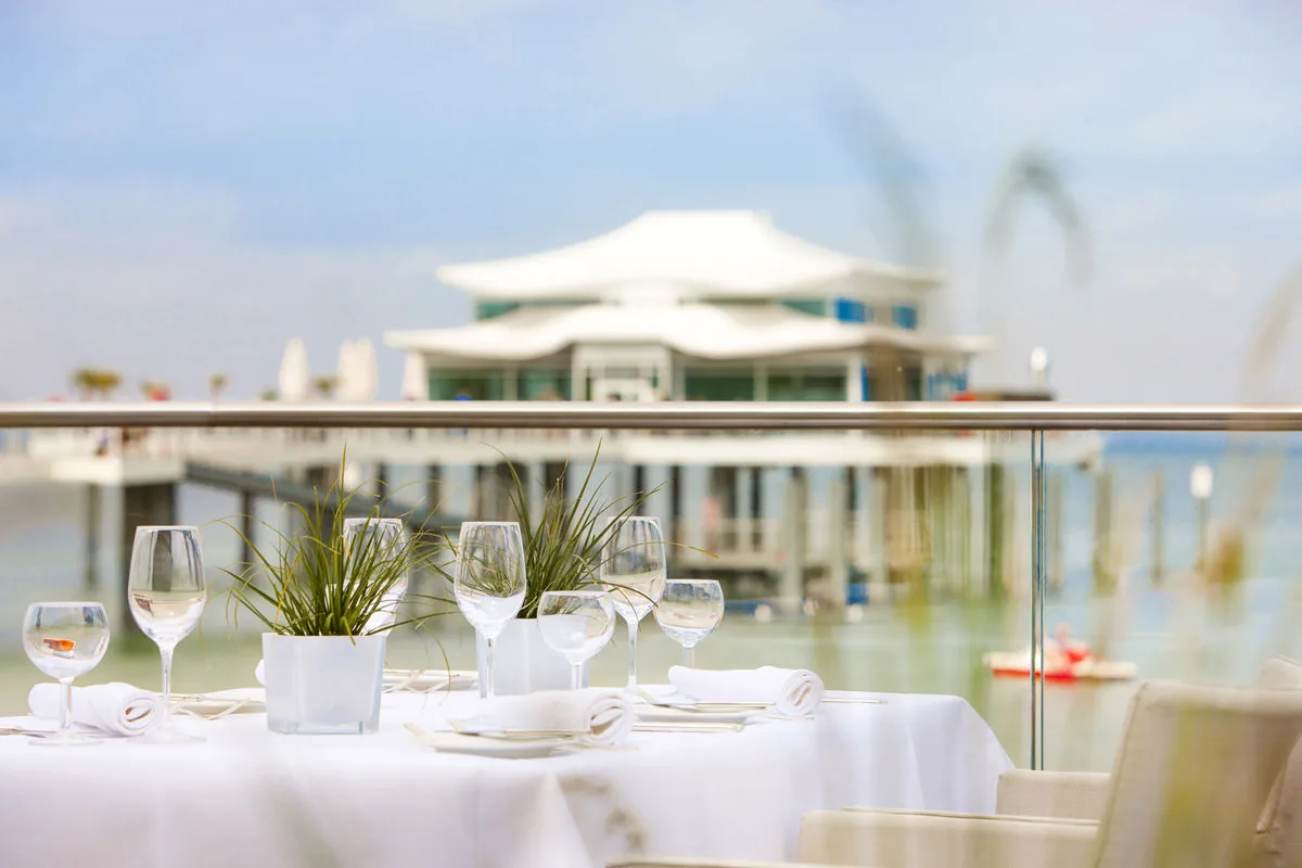 Weiß eingedeckter Tisch auf der Terrasse mit Blick auf die Seebrücke und das Meer