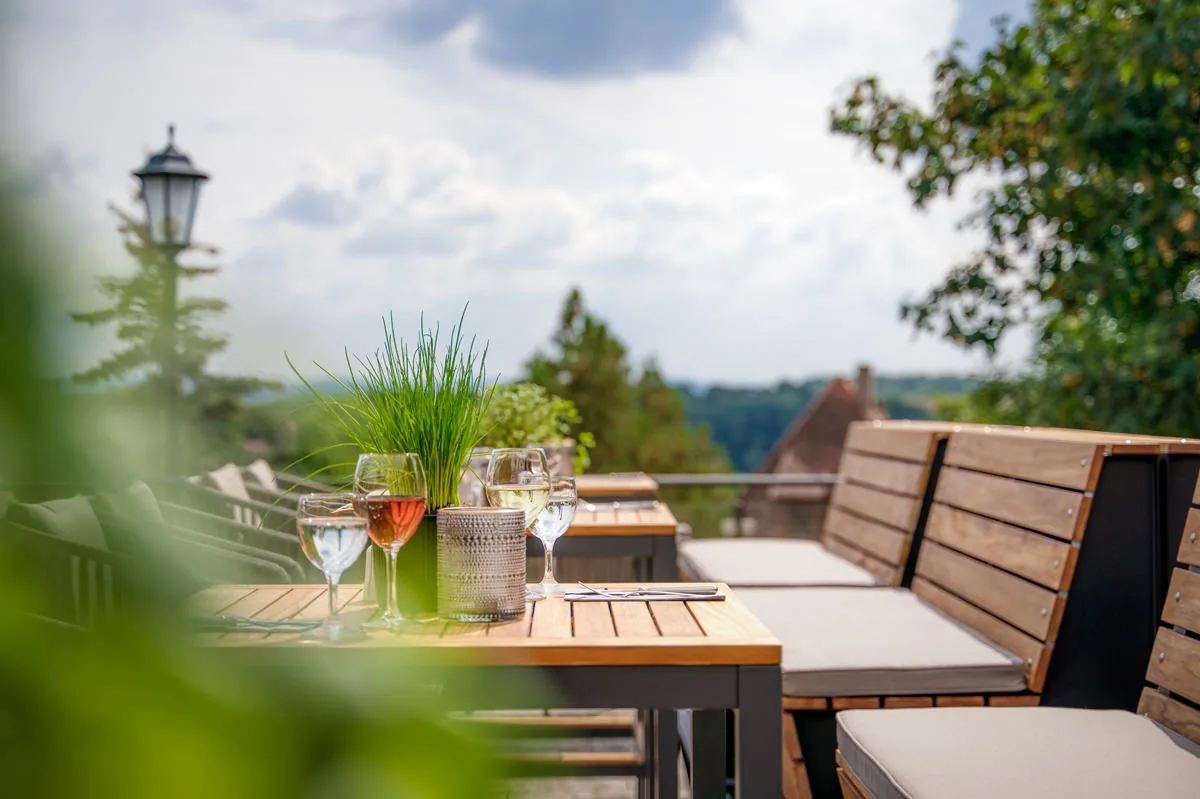 Gedeckter Tisch auf der Terrasse mit Weingläsern und Blick über die bewaldete Landschaft
