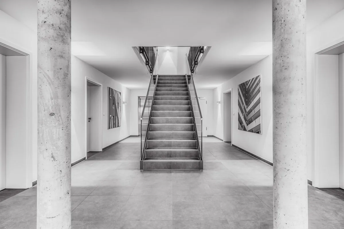 Treppenhaus in Schwarzweiß – symmetrischer Blick zwischen zwei Betonstützen auf die Treppe