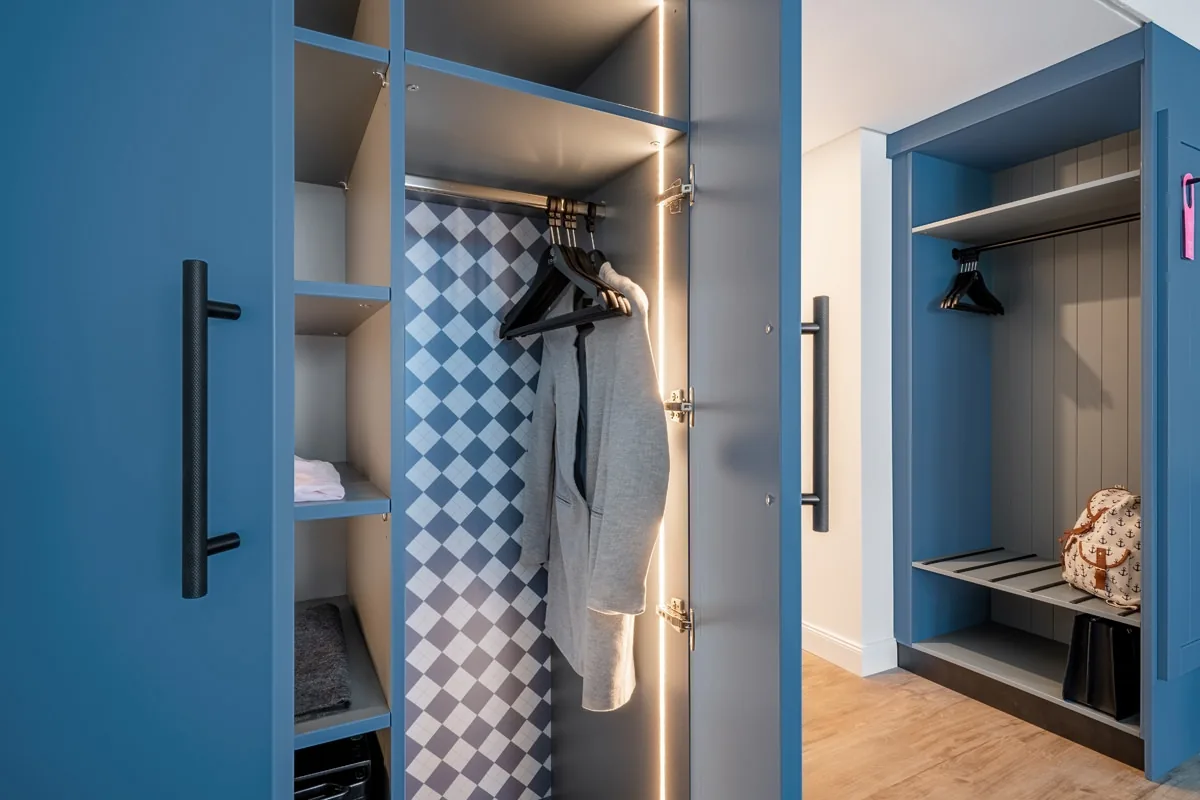 Offener Kleiderschrank im Hotelzimmer mit Bademantel, Ablagefächern und beleuchteter Garderobe